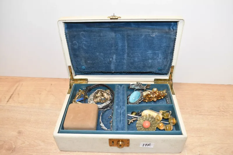 A cream faux leather jewellery box, containing an assortment of costume jewellery, including faux pearls, shell necklaces and statement brooches