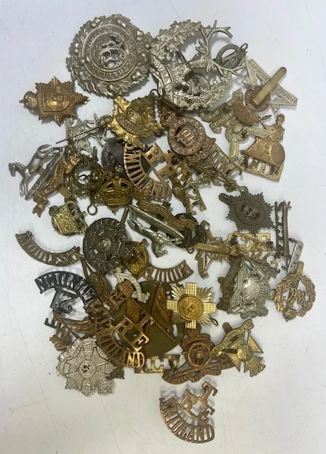 A large collection of early 20th century cap badges, collar badges and shoulder titles to include Wiltshire regiment, Essex Yeomanry, Lowland regiment